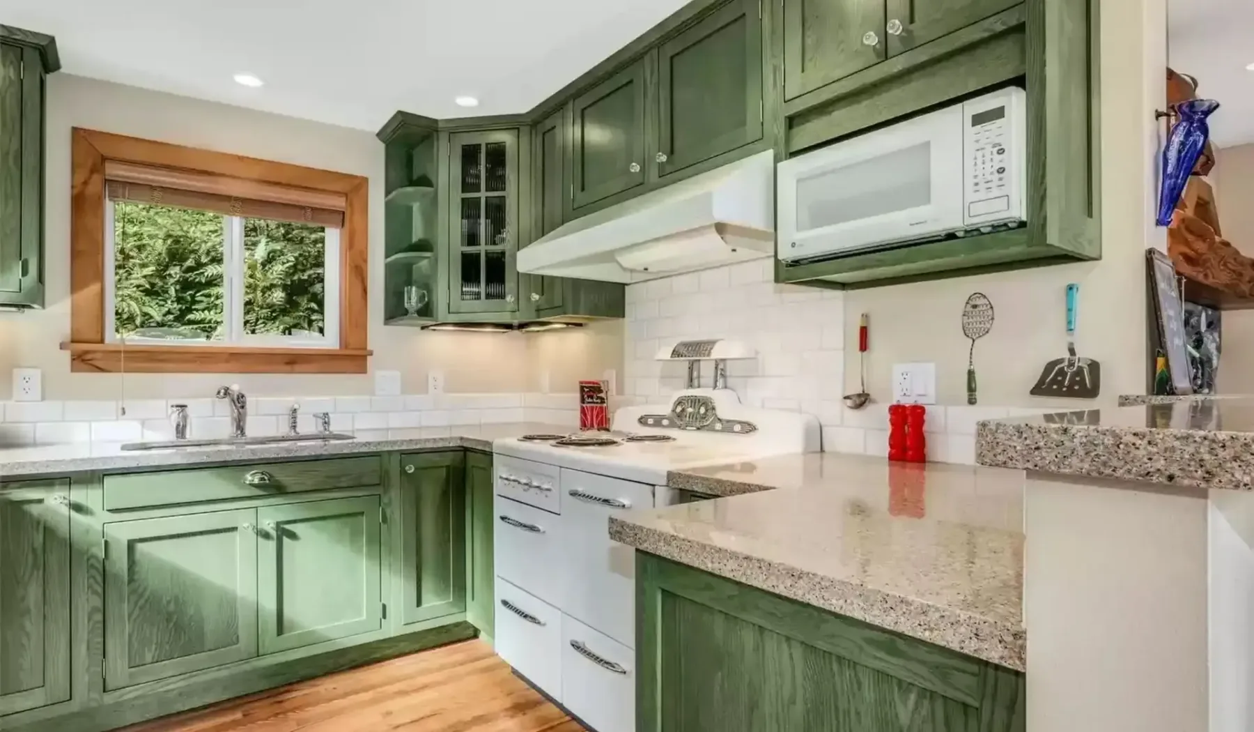 Una cocina con gabinetes verdes, electrodomésticos blancos y una amplia encimera.