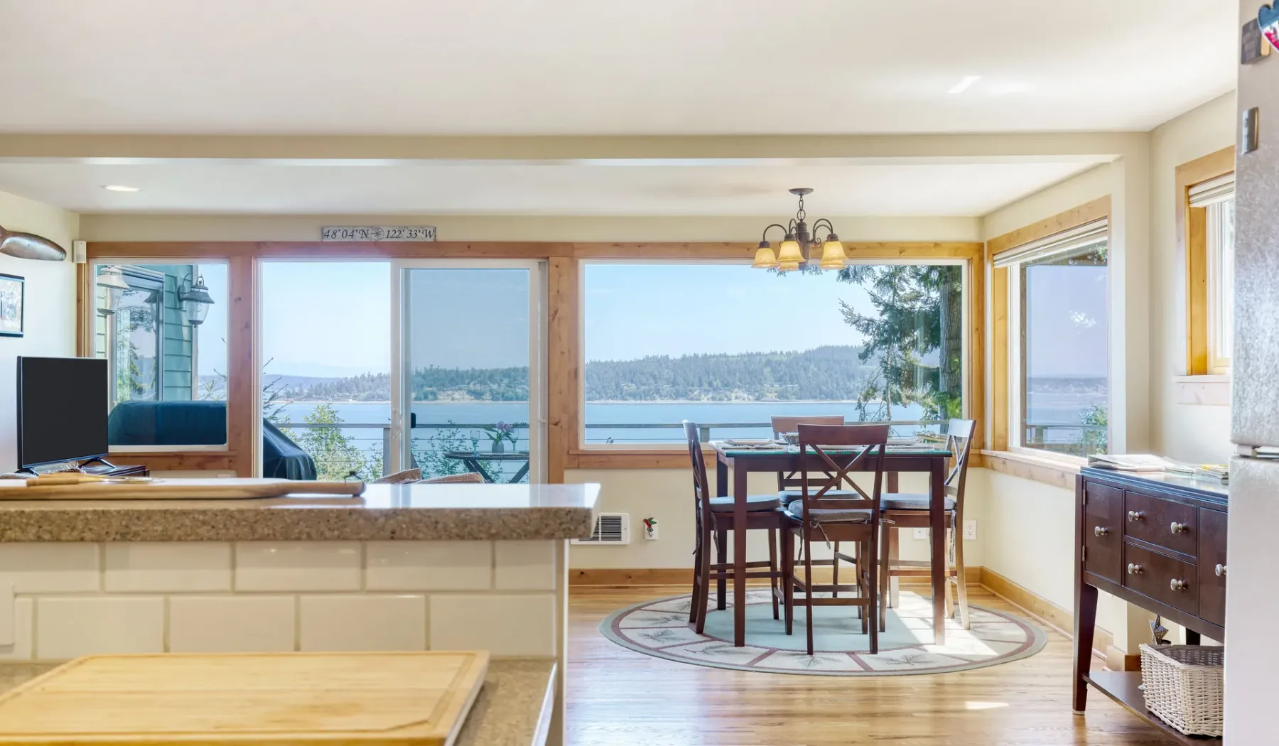 Un comedor luminoso con una mesa de madera junto a grandes ventanas con vistas al agua.