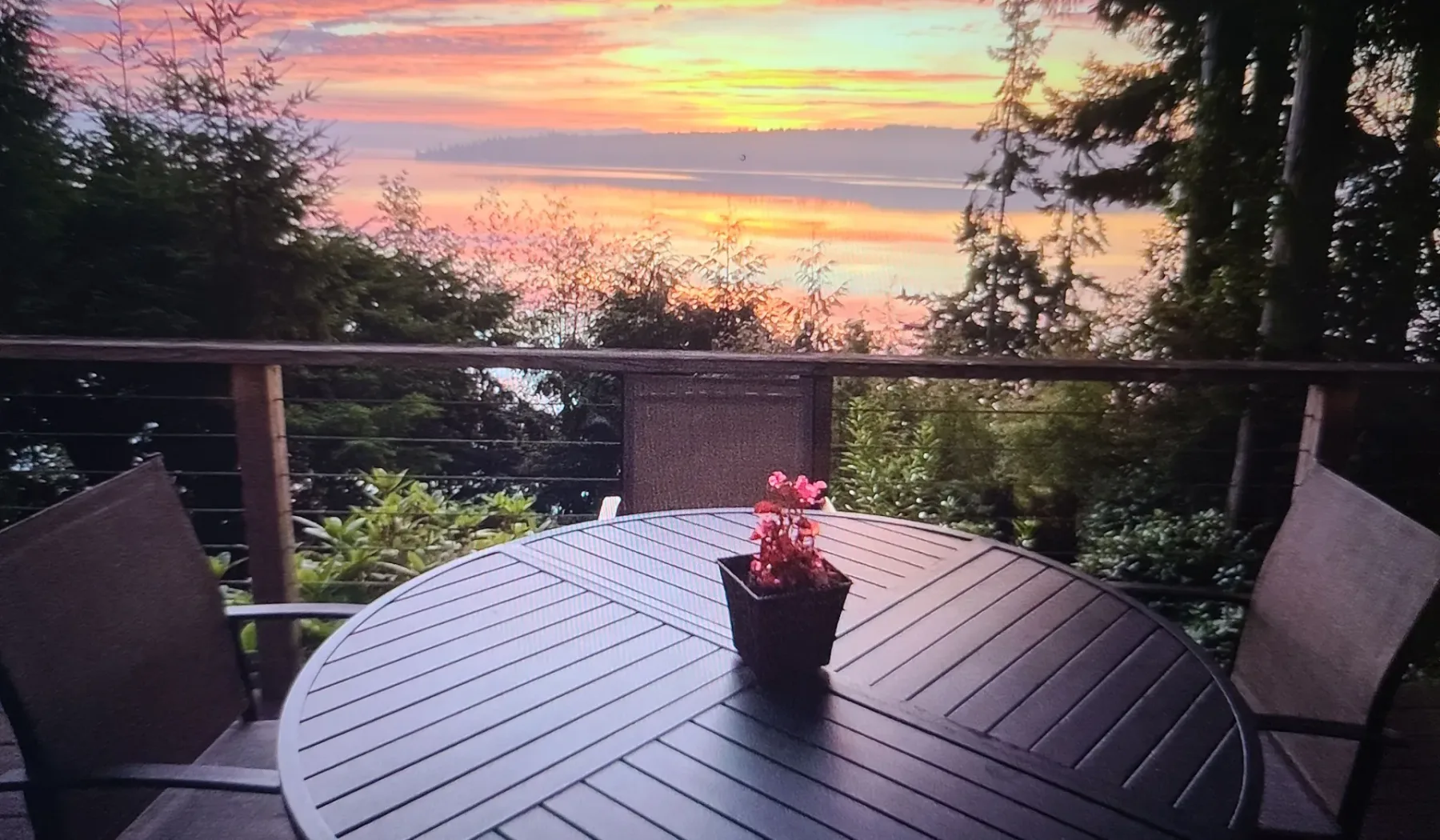 Una mesa y sillas de patio miran hacia los árboles bajo un cielo colorido al atardecer.