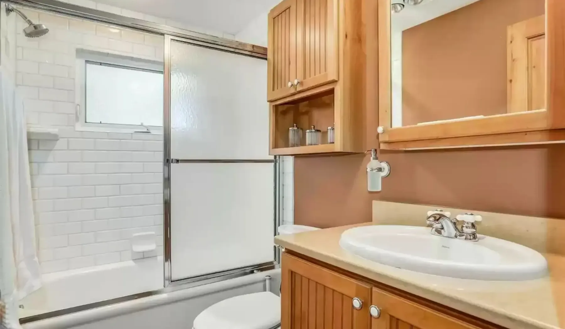 Un baño con lavabo, mueble de madera y zona de ducha con azulejos.