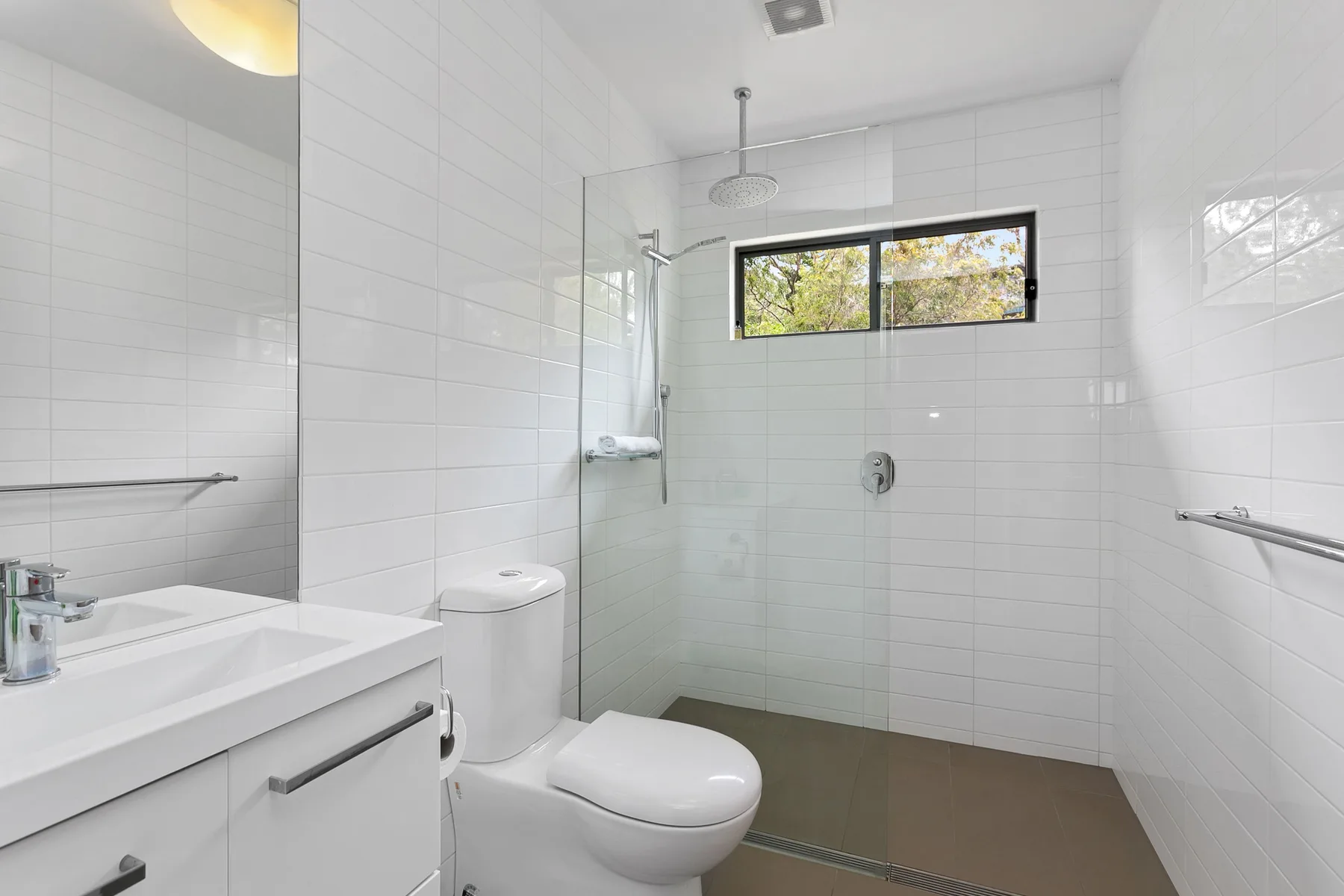 Baño luminoso con azulejos, ducha, inodoro y lavabo.