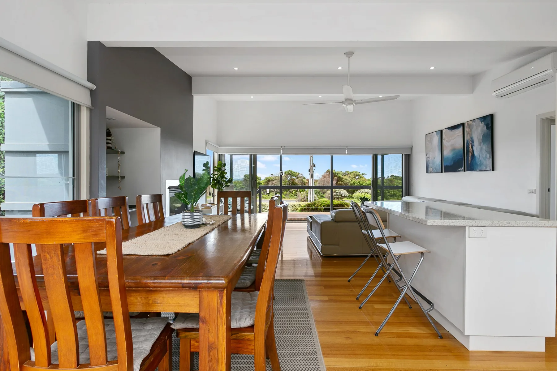 Comedor y sala de estar de planta abierta con una larga mesa de madera y grandes ventanas.