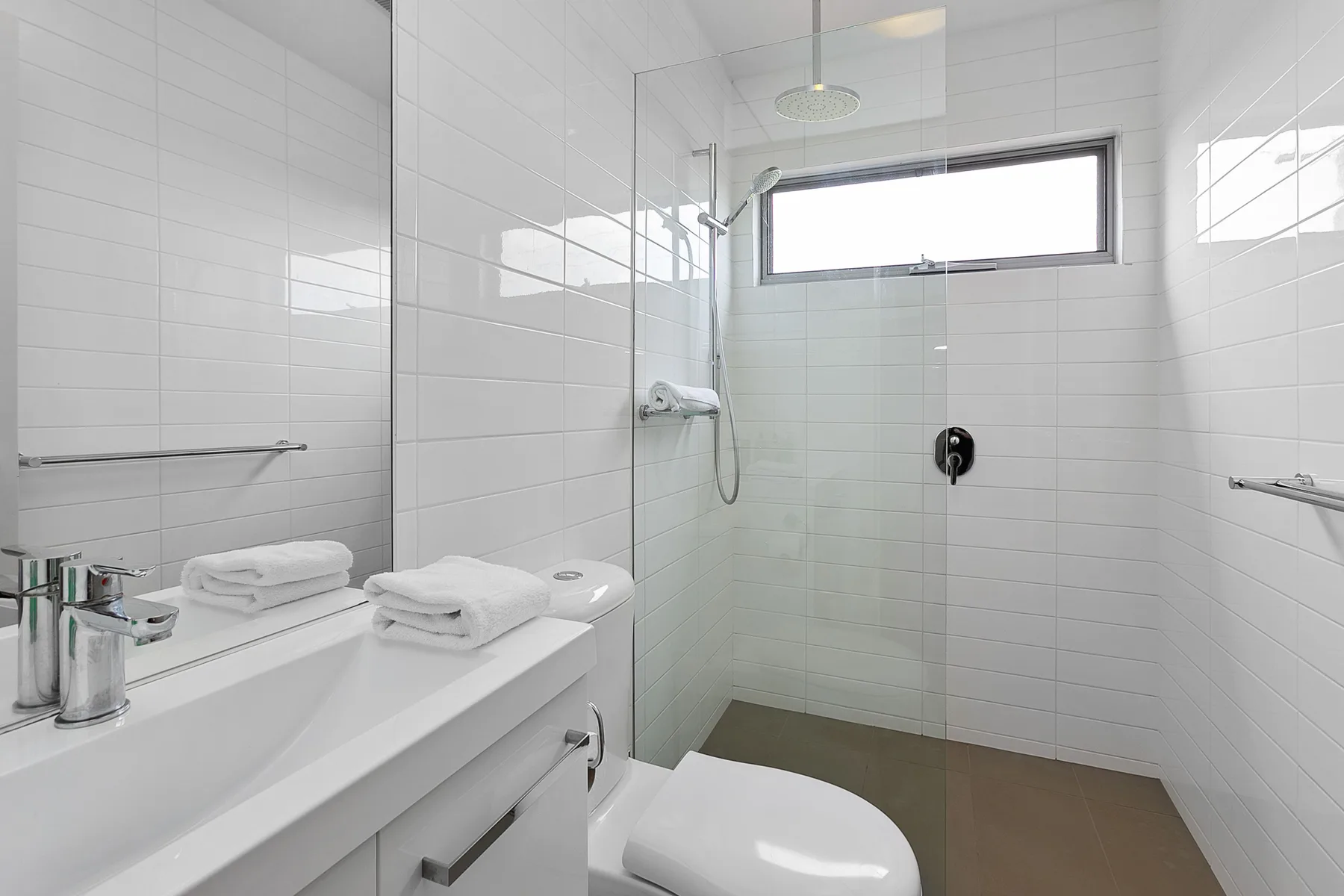 Un baño luminoso con azulejos, ducha de vidrio y lavabo blanco.
