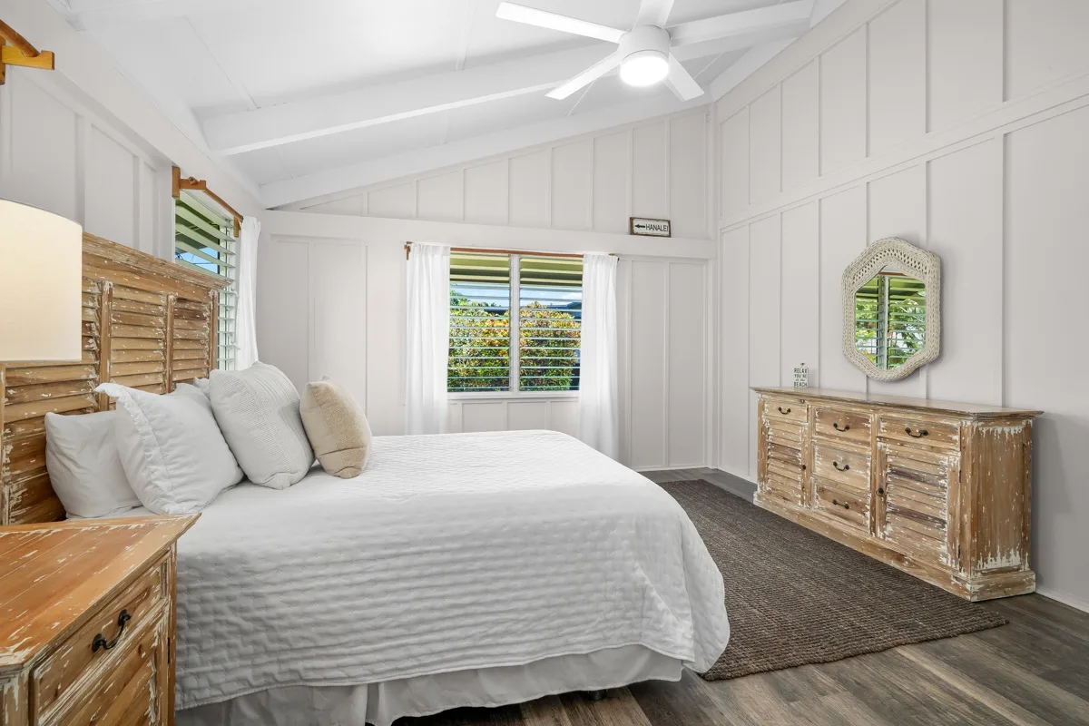 Un dormitorio luminoso con una cama, cómodas de madera y una ventana con vistas a la vegetación.