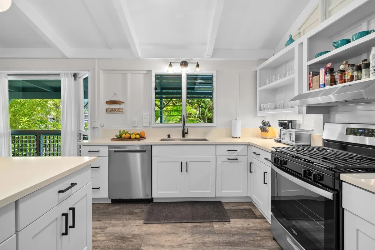 Una cocina luminosa con gabinetes blancos, una ventana central y una estufa negra.