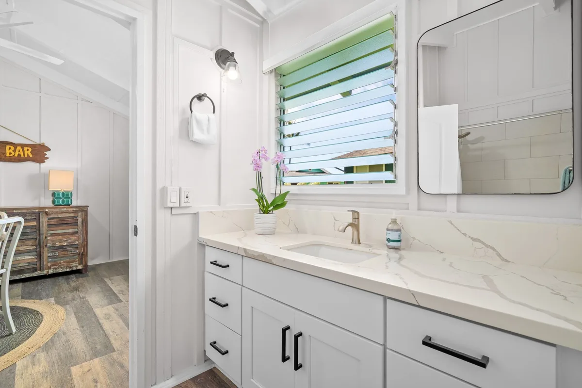Un lavabo de baño luminoso está bajo una ventana con persianas verdes.