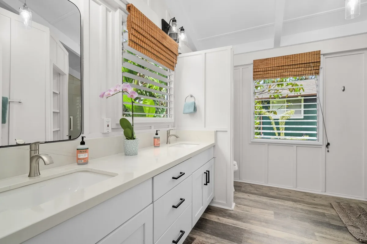 Un tocador de baño luminoso con lavabo, espejo y ventanas con persianas de bambú.