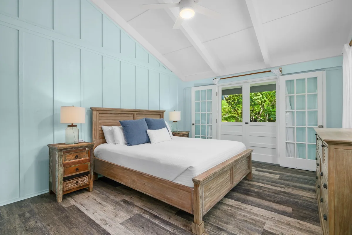 Un dormitorio con una cama de madera, ropa de cama blanca y paredes celestes con paneles.