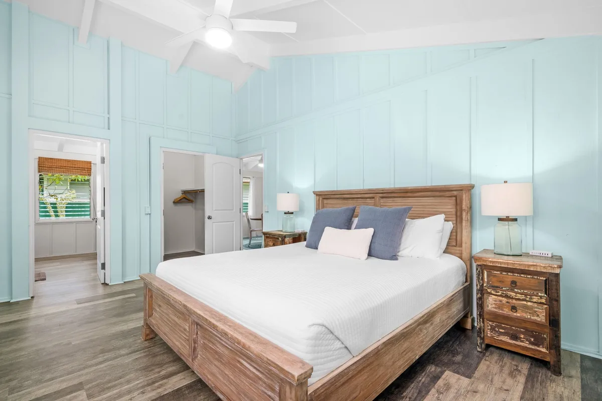Un dormitorio con una cama de madera, mesitas de noche y paredes paneladas de color azul claro.