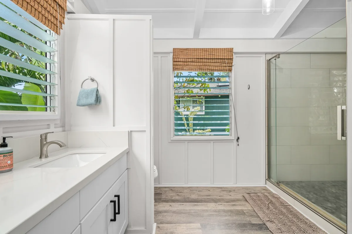 Un baño luminoso con tocador blanco, ventana y ducha de vidrio.