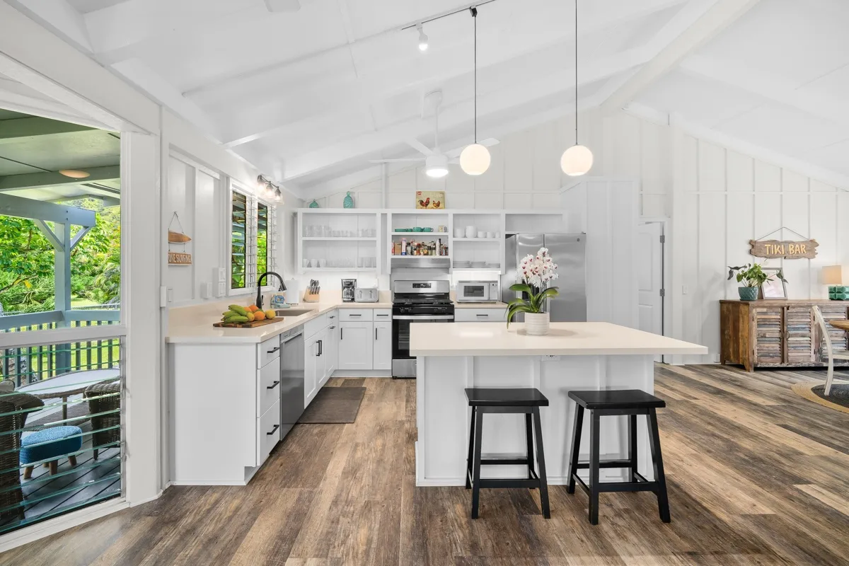 Una cocina luminosa con gabinetes blancos, una isla central y piso de madera.