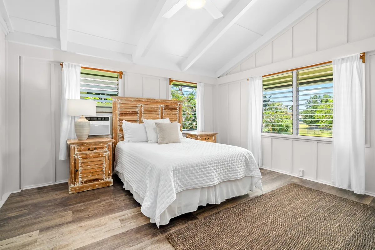 Un dormitorio luminoso con una cama blanca y ventanas con vista a la vegetación.