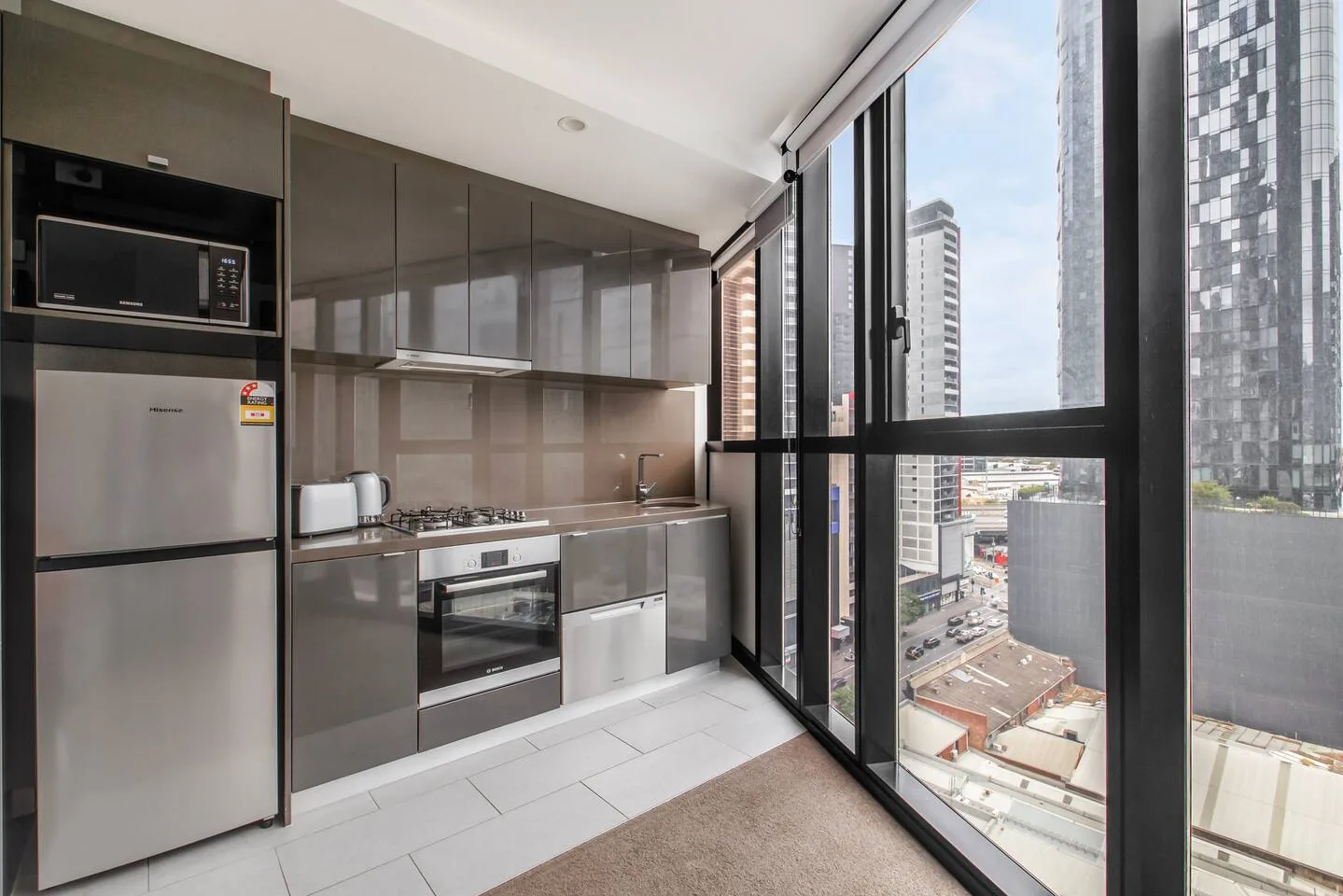 Una cocina moderna con gabinetes oscuros y grandes ventanas con vistas a edificios de la ciudad.