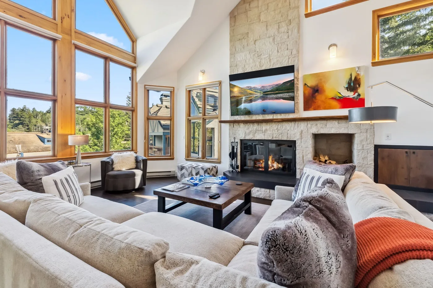 Una sala de estar luminosa con chimenea de piedra y grandes ventanas.