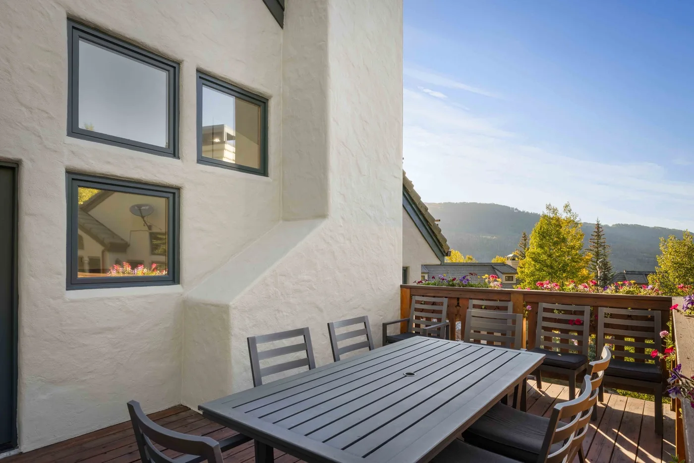 Una zona de comedor al aire libre con mesa y asientos da a un paisaje montañoso.