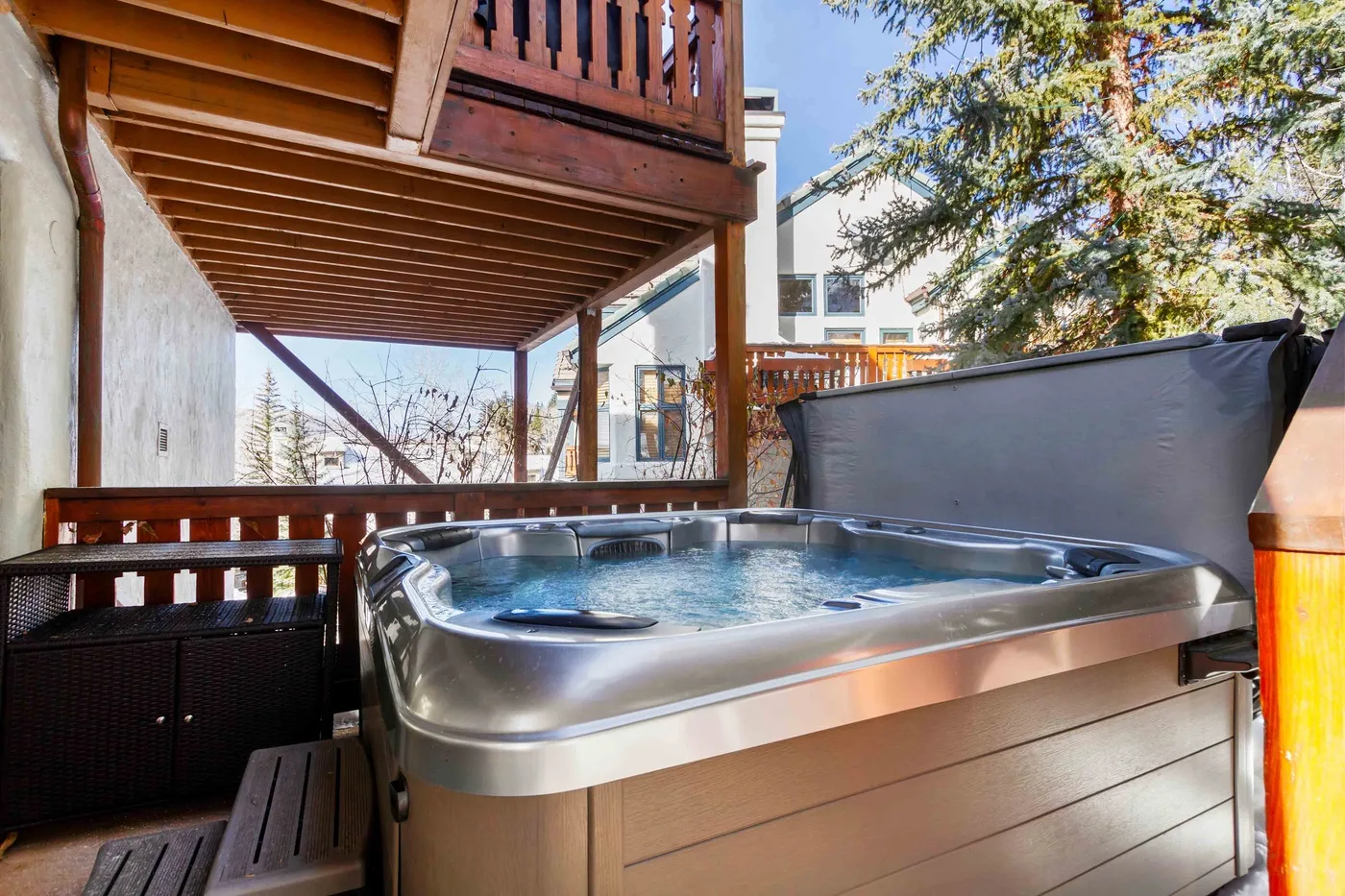 An outdoor hot tub sits beneath a wooden deck beside a privacy screen.