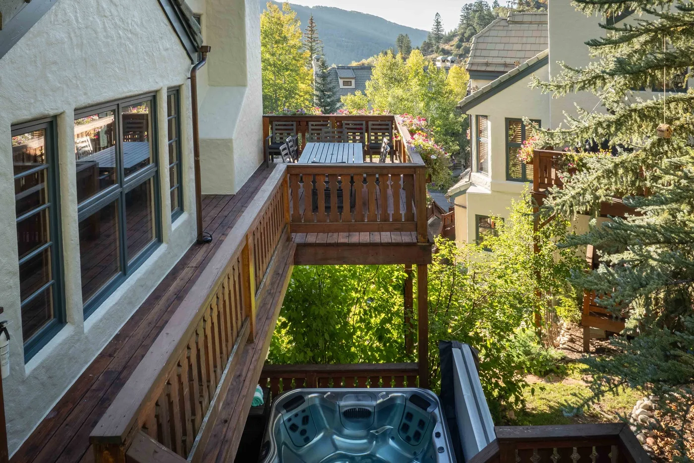 Una terraza exterior da a una ladera arbolada, con una bañera de hidromasaje debajo.