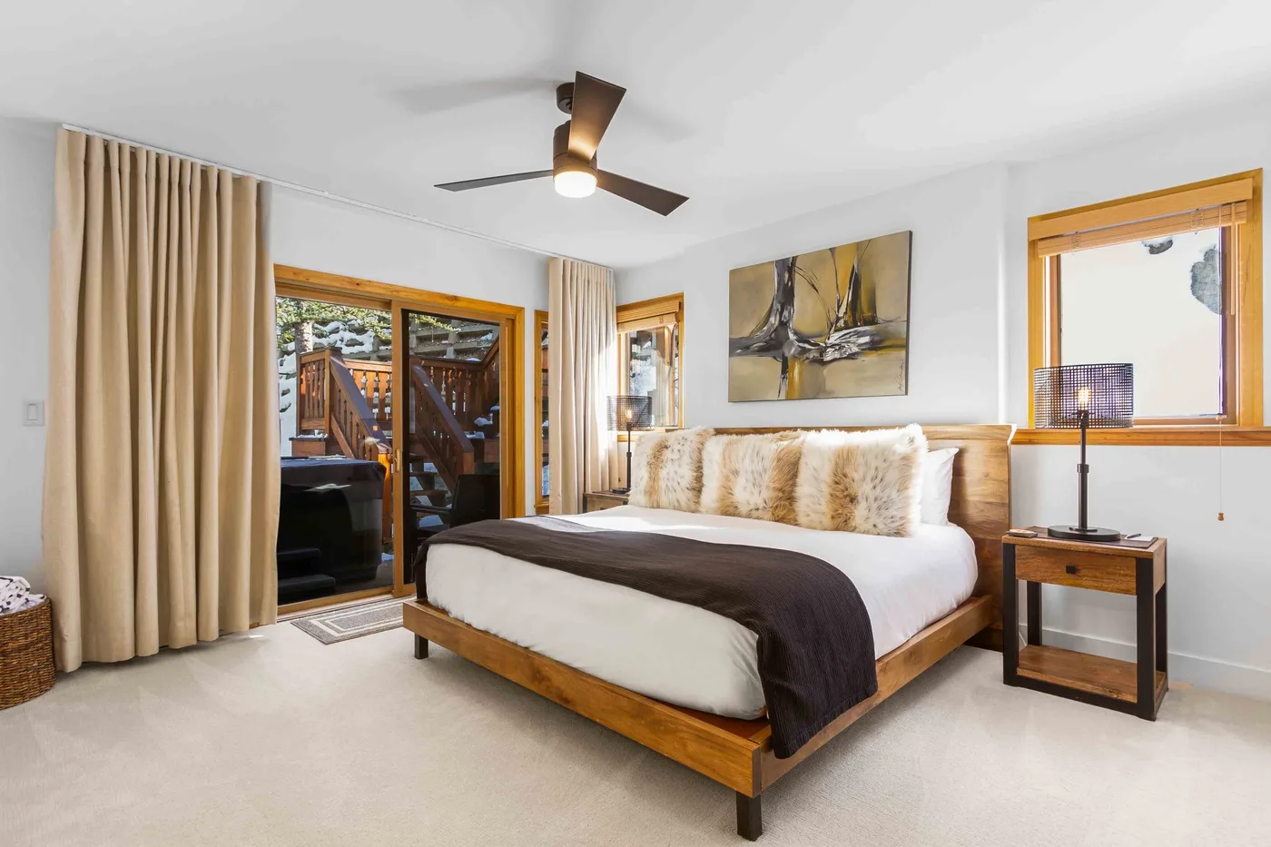 Un dormitorio con una cama de madera, ropa de cama clara y cortinas junto a una puerta de vidrio.