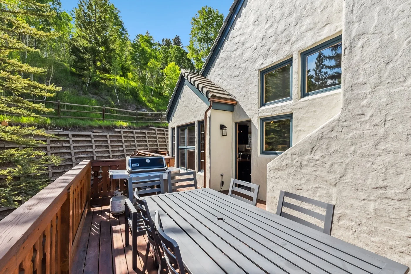 Una terraza exterior junto a una casa tiene una mesa de comedor y una parrilla.
