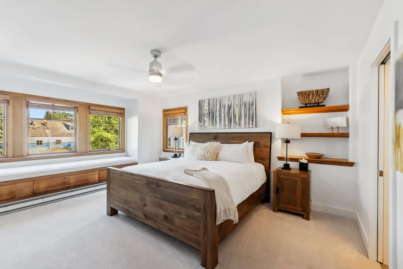 Un dormitorio luminoso con una cama de madera y un amplio asiento junto a la ventana.