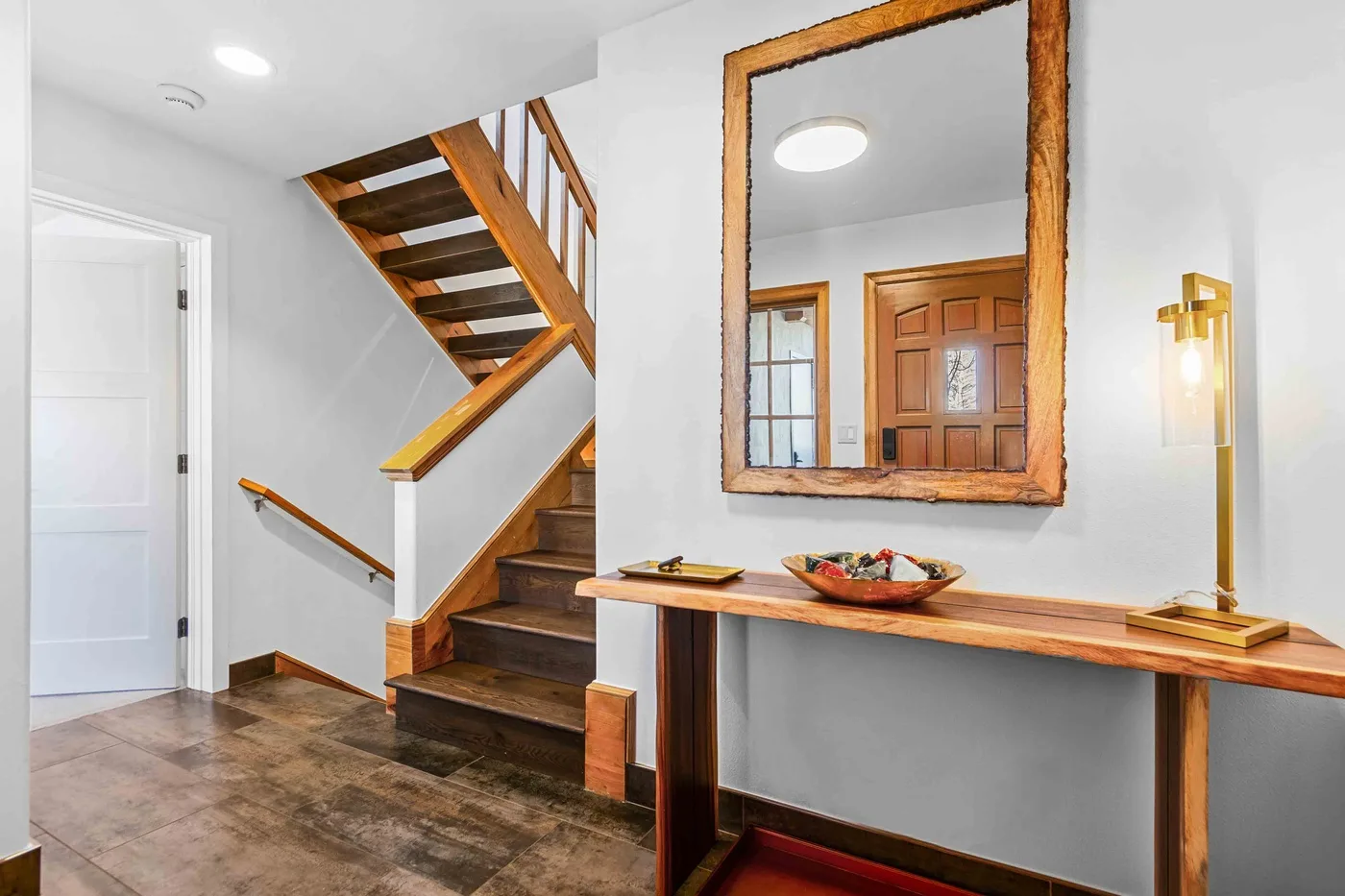 Un recibidor luminoso con una escalera de madera y una consola larga bajo un espejo.