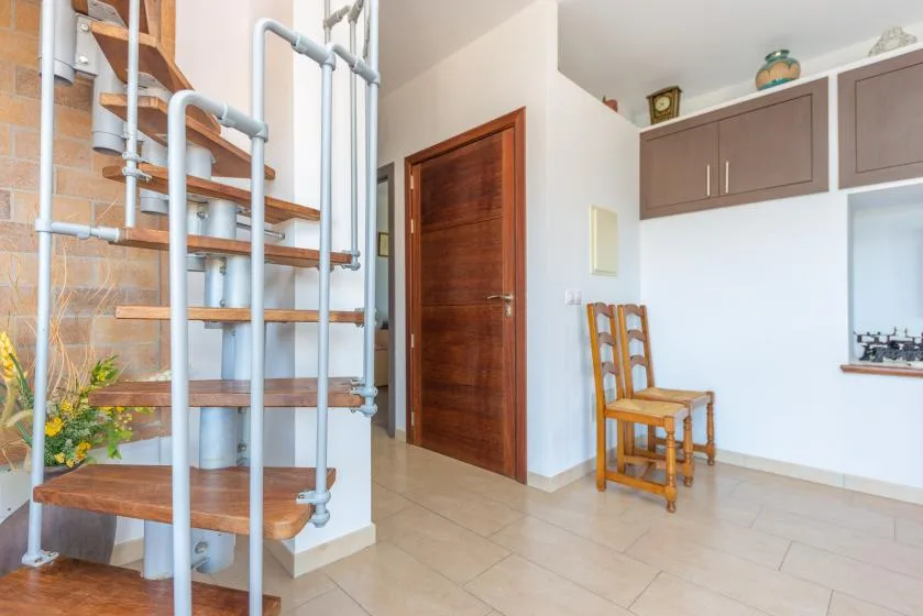 Un interior luminoso con una escalera de madera, una puerta y una silla.
