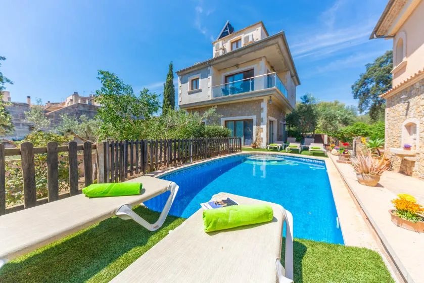 Una piscina al aire libre junto a una casa, con tumbonas a un lado.