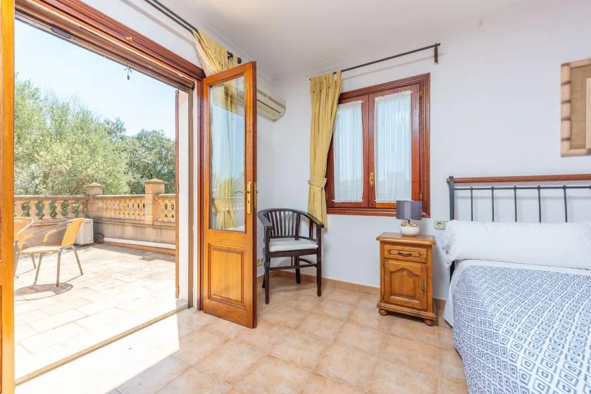 Un dormitorio se abre a una terraza soleada a través de una puerta acristalada con marco de madera.