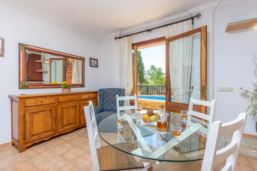 Un comedor con una mesa de vidrio y una puerta abierta con vistas a la vegetación.