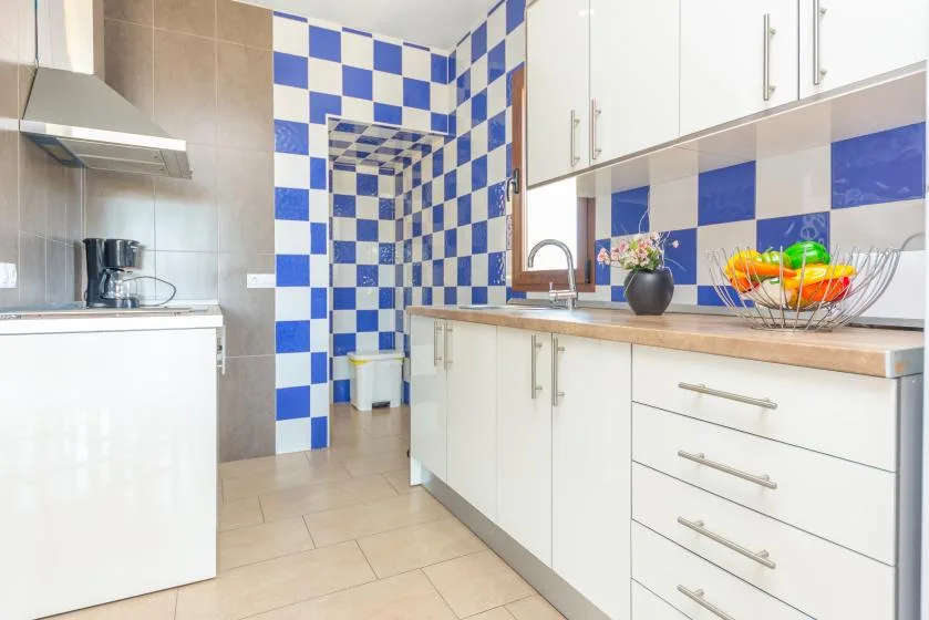 Una cocina luminosa con gabinetes blancos y paredes de azulejos azules y blancos.