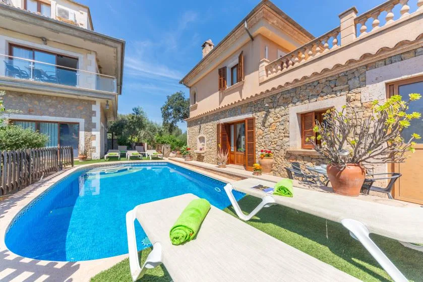 Una piscina exterior está junto a una casa de piedra y estuco, con tumbonas cerca.
