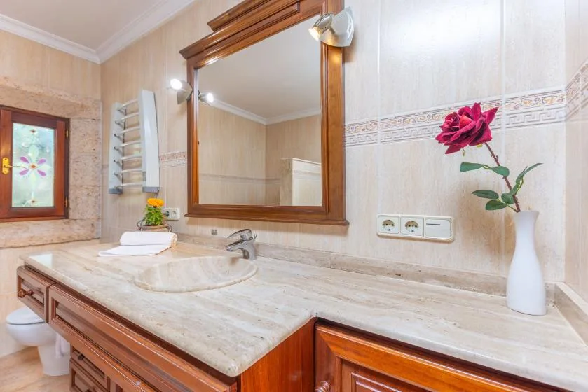 Un lavabo de baño con un espejo grande y una flor en un jarrón.
