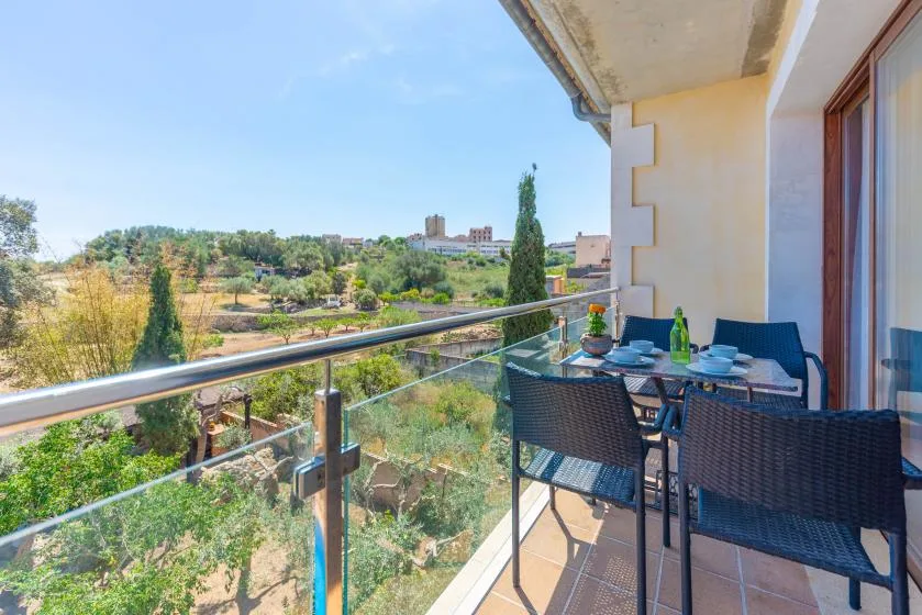 Una zona de comedor en el balcón da a árboles verdes y terreno abierto.