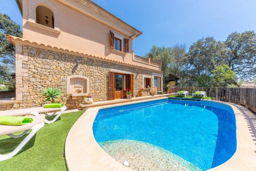 Una piscina curva junto a una casa de dos plantas y asientos al aire libre.