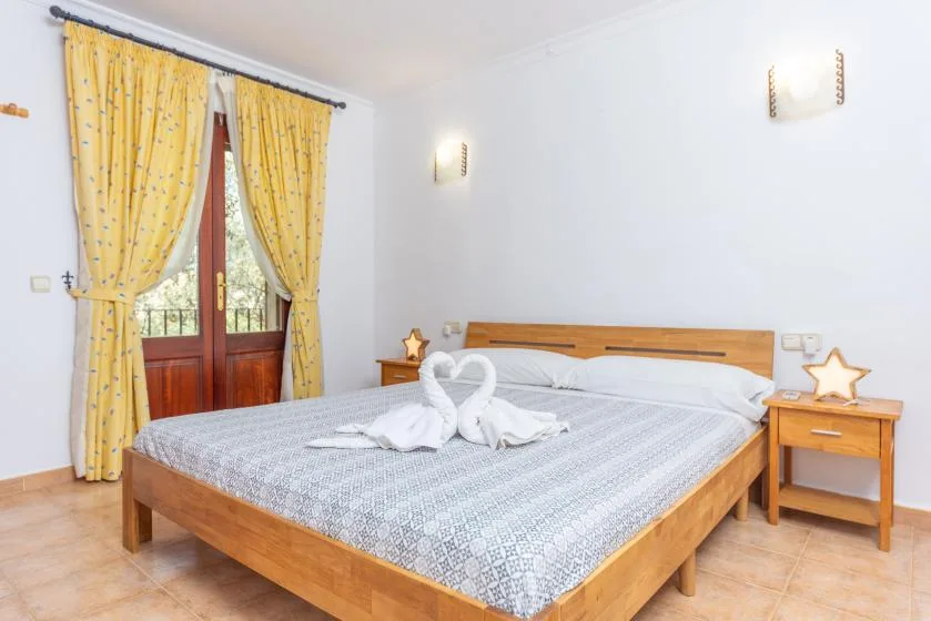 Un dormitorio con una cama de madera y cortinas amarillas junto a una puerta acristalada.