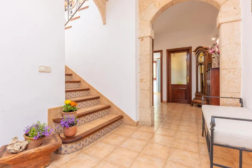 Una entrada interior con una escalera de baldosas, flores en macetas y un pasaje en arco.