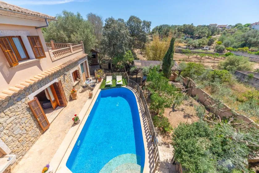 Una piscina junto a una casa, con vegetación y campos al fondo.