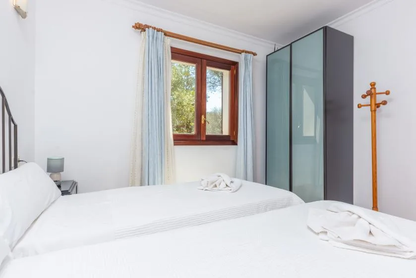 Dormitorio con ropa de cama blanca, una ventana con cortinas y un armario.