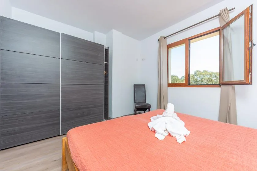 Un dormitorio con una cama de color coral, un armario oscuro y una ventana abierta.