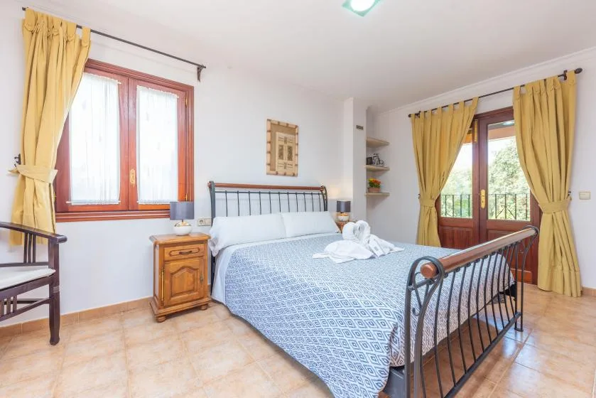 Un dormitorio con una cama de metal, cortinas amarillas y puertas acristaladas que dan a un balcón.