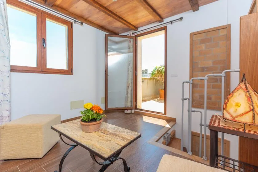 Una luminosa zona de estar tiene una mesa baja, asientos acolchados y una puerta de cristal abierta.