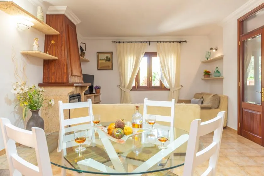 Comedor con mesa de cristal y asientos junto a una sala de estar luminosa.