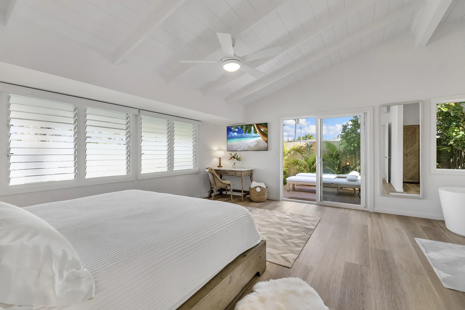A bright bedroom with a large bed, desk, and sliding glass doors.