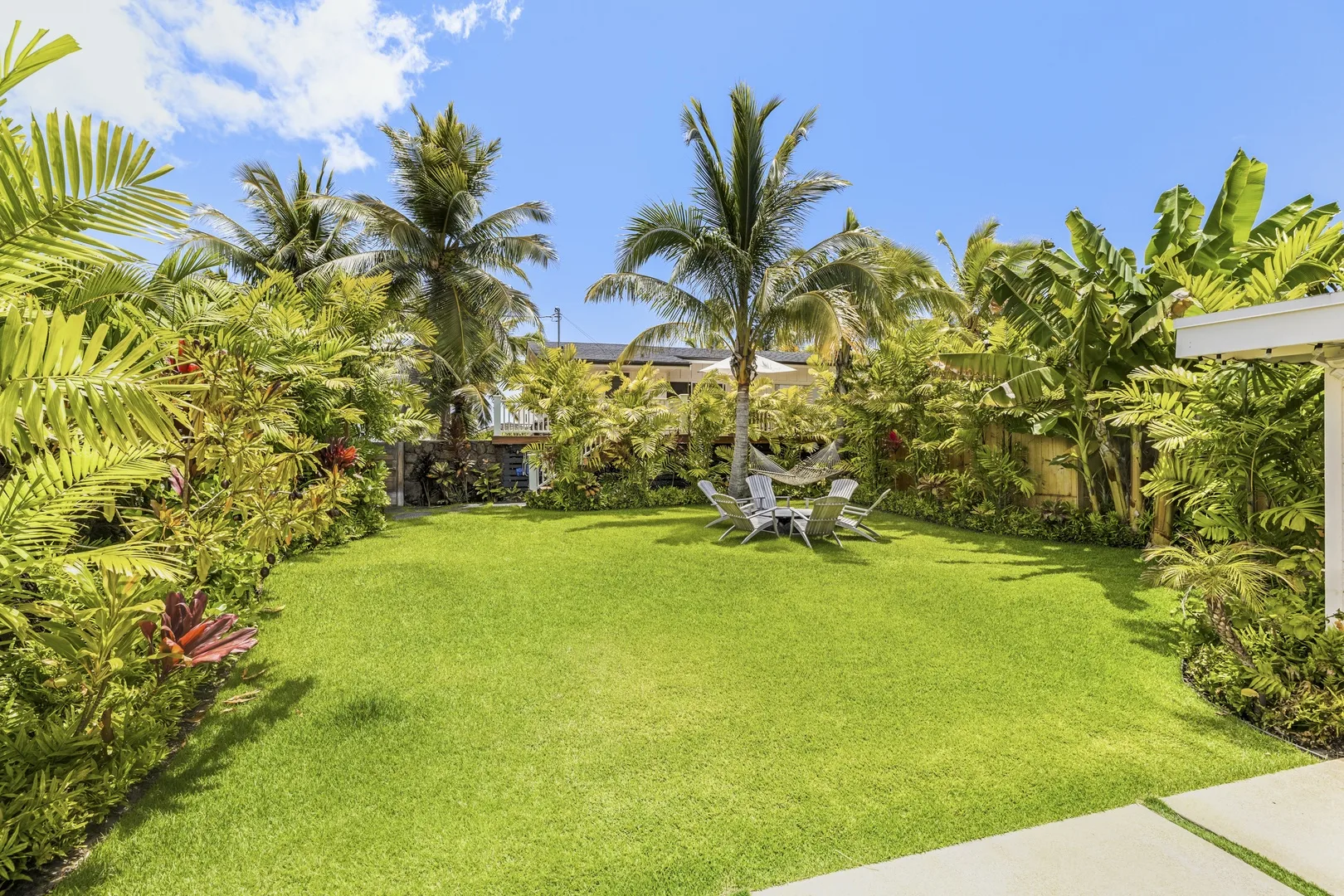 A tropical garden with a broad lawn, lush plants, and outdoor seating.