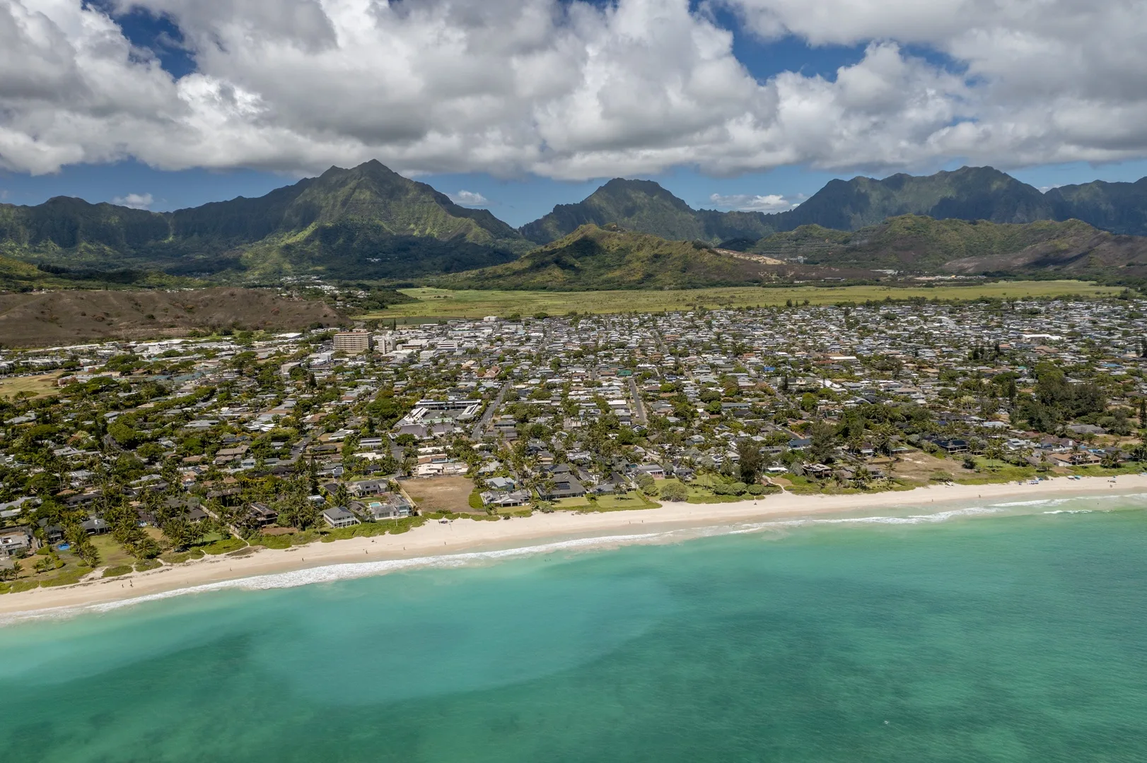 Aerial view of a coastal town beside a sandy beach, with mountains in the distance.