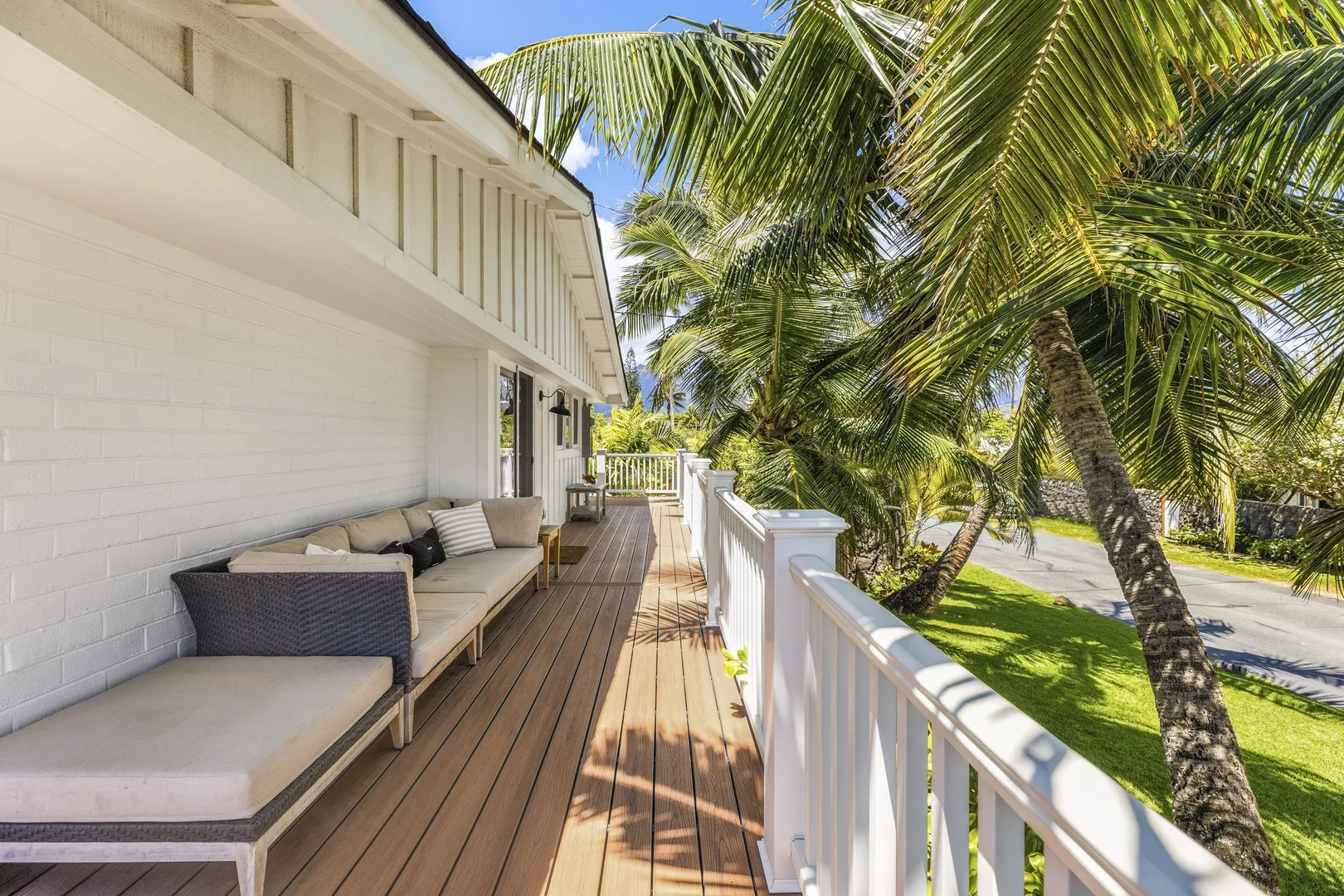 A wooden deck with cushioned seating overlooks a white railing and palm trees.
