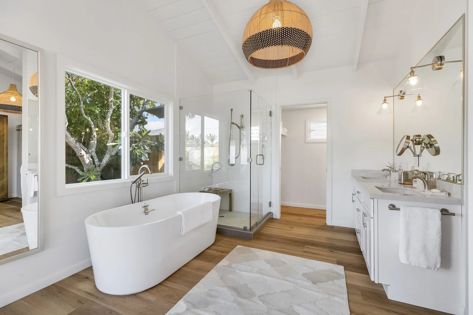 A bright bathroom features a freestanding bathtub, glass shower, and vanity.