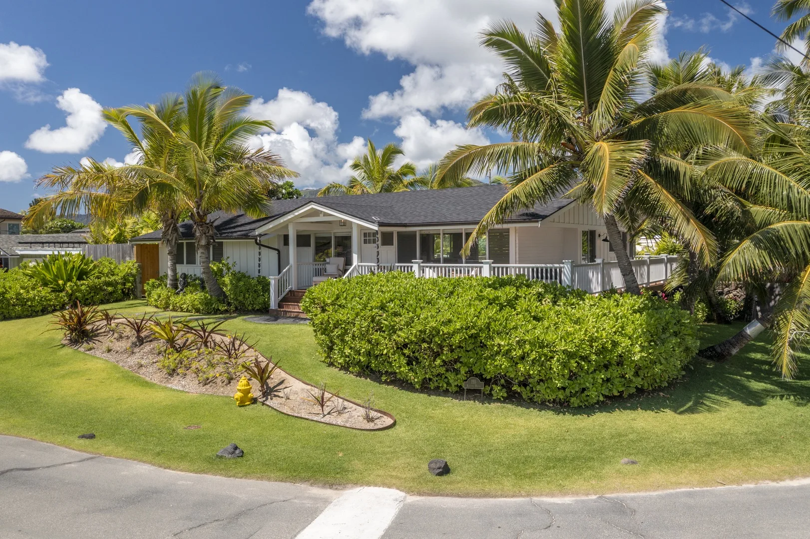 A single-story house with a covered porch stands behind a landscaped lawn and hedges.