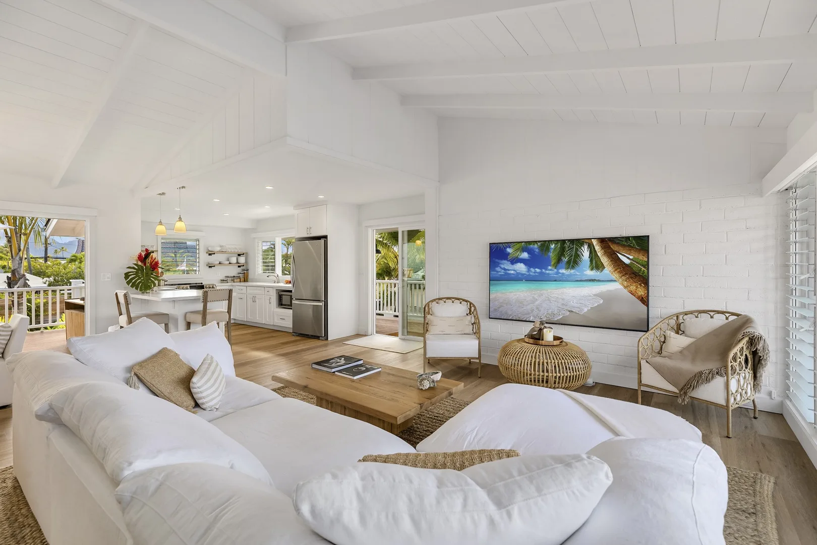 A bright open-plan living room with white seating and a kitchen beyond.