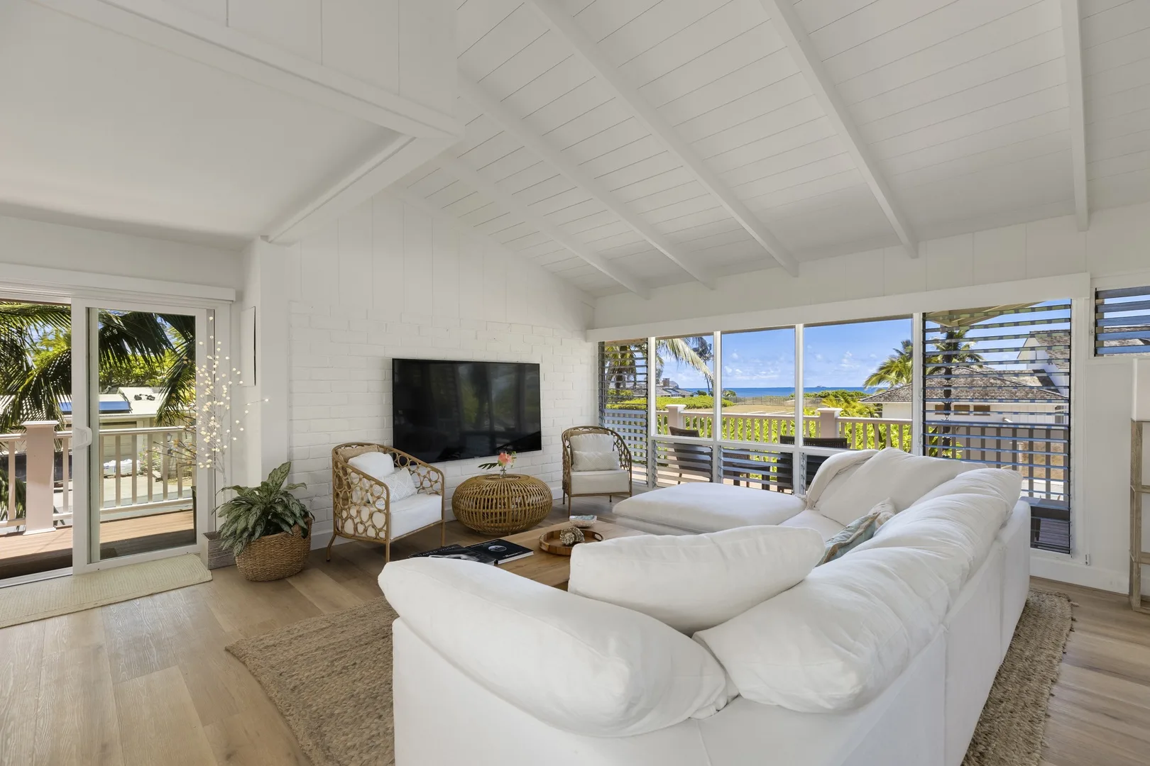 A bright living room has white seating, a television, and wide windows overlooking the water.